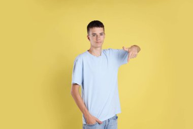 Sarı arka planda açık mavi tişört giyen genç çocuk.