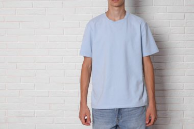 Beyaz tuğla duvarın yanında açık mavi tişört giyen genç çocuk, yakın plan. Metin için boşluk