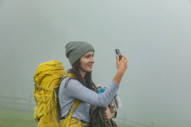 Sırt çantalı genç yürüyüşçü puslu dağlarda selfie çekiyor.