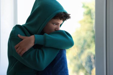 Yalnızlık kavramı. Pencerenin yanındaki üzgün genç çocuk.