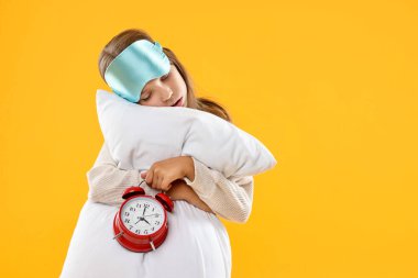 Uyku maskesi, yastık ve alarm saati turuncu arka planda uyuyakalan kız, mesaj için yer