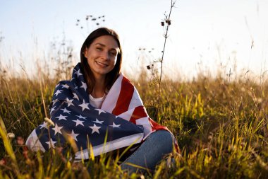 Amerika bayrağını taşıyan mutlu kadın çimlerin üzerinde oturuyor. Metin için boşluk