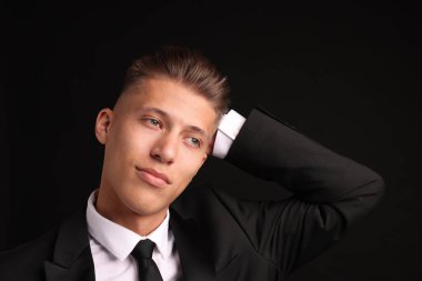 Siyah arka planda şık saç kesimi olan kendine güvenen genç bir adam.