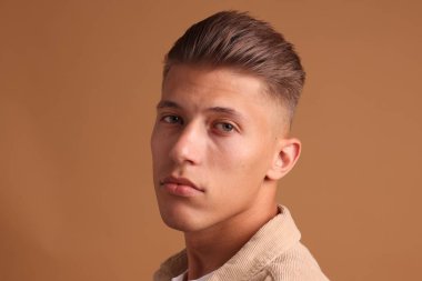 Kahverengi arka planda şık saç kesimi olan kendine güvenen genç bir adam.