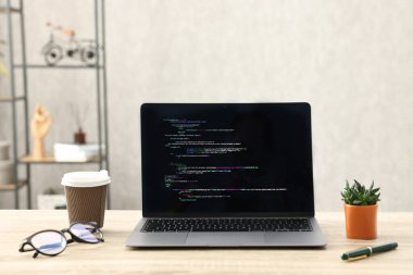 Programcının işyeri. Tamamlanmamış kodu olan modern bir bilgisayar, kağıt bardak, bardak ve ev bitkisi.