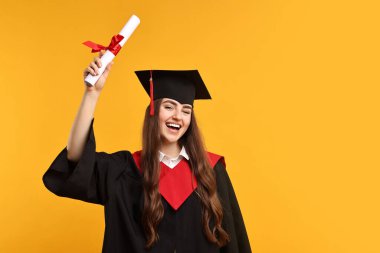Mezun olduktan sonra turuncu arka planda diploması olan mutlu bir öğrenci. Metin için boşluk