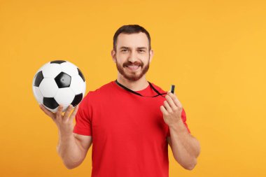 Islık çalan ve turuncu arka planda futbol topu olan mutlu genç adam.