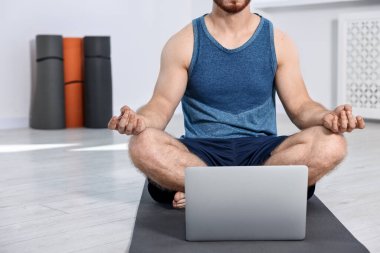 Evdeki yoga minderinde dizüstü bilgisayarın yanında meditasyon yapan bir adam. Metin için boşluk