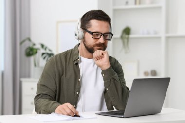 Interpreter in headphones having video chat via laptop at white table indoors clipart