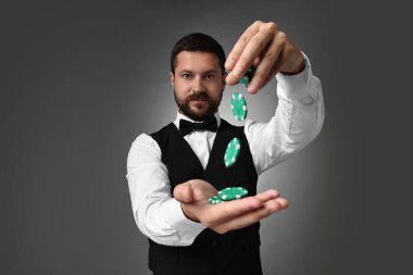 Gri arka planda kumarhane fişleri olan krupiye.