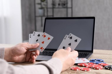 Çevrimiçi poker. Oyun kartları, cipsleri ve laptopu olan adam ahşap masada, yakın plan.