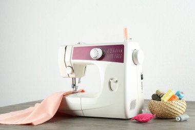 Beyaz arka plana karşı ahşap masa üzerinde kumaş ve araçlar ile bir dikiş makinesi