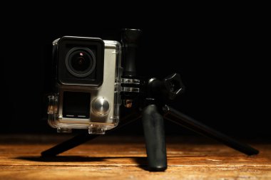 Ahşap zemin üzerinde modern aksiyon kamerası ve tripod siyah arkaplan karşı