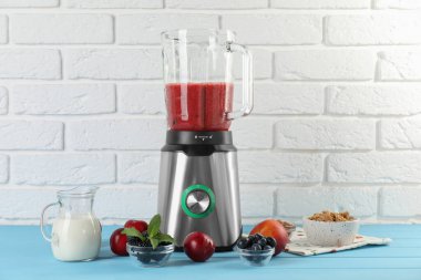 Açık mavi ahşap masa üzerinde malzemelerin ve diğer taze ürünlerin karışımıyla karıştırıcı