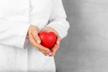 Doktor gri arka planda kırmızı kalbi tutuyor, yakın plan. Metin için boşluk