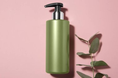 Pembe arka planda bir şişe şampuan ve okaliptüs dalı.