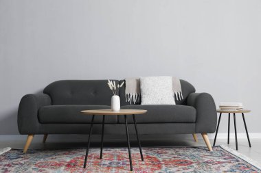 Rahat bir kanepe ve gri duvarın yanındaki masalar.