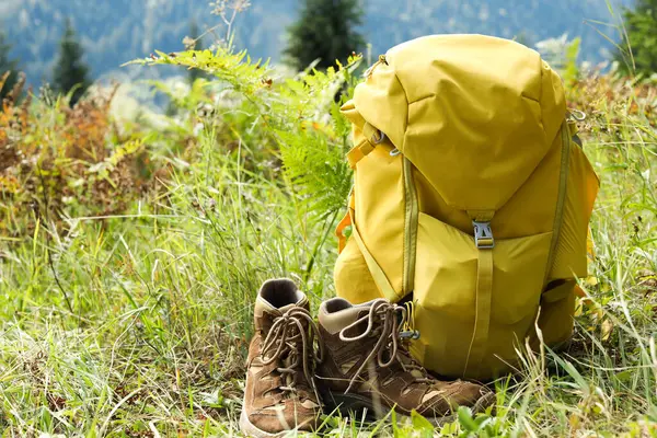 Yeşil çimlerin üzerinde sırt çantası ve yürüyüş ayakkabıları.