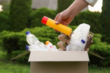 Geri dönüşüm konsepti. Dışarıdaki karton kutuya plastik şişe koyan adam.