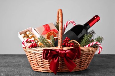 Şarap dolu hasır bir hediye sepeti ve gri desenli bir Noel süsü.