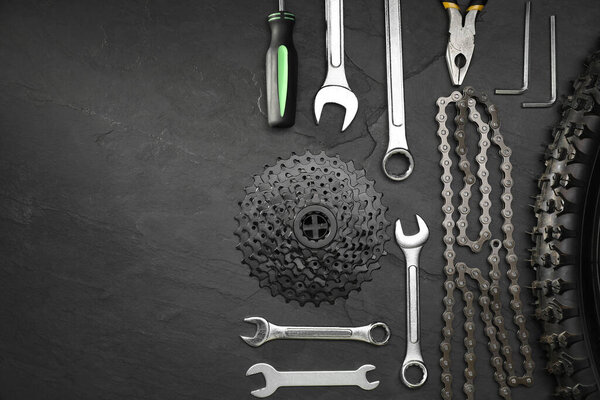 Parts of bicycle and tools on black table, flat lay. Space for text