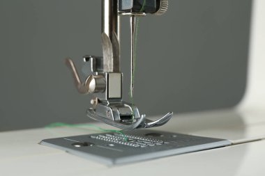 Gri arkaplanda yeşil iplikli dikiş makinesi, yakın plan