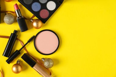 Sarı zemin üzerinde makyaj ürünleri ve Noel dekoru olan düz konum, metin için boşluk