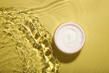 Sarı arka planda kremalı kavanoz, üst manzara. Kozmetik ürünü