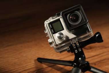 Ahşap yüzeyde modern aksiyon kamerası ve tripod, yakın plan.