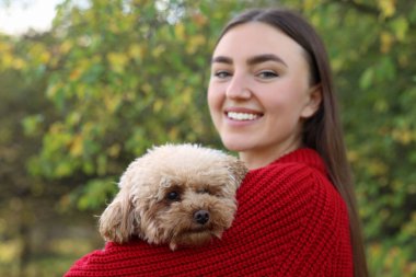 Sonbahar parkında sevimli köpeğiyle gülümseyen kadın.