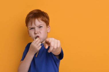 Turuncu arka planda ıslık çalan küçük çocuk, mesaj için boşluk