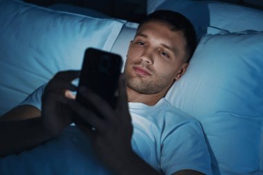 Kötü alışkanlık. Adam gece yatakta akıllı telefon kullanıyor.