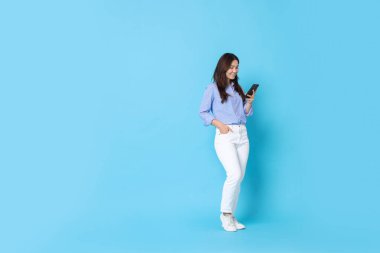 Açık mavi arka planda akıllı telefon kullanan gülümseyen kadın. Metin için boşluk