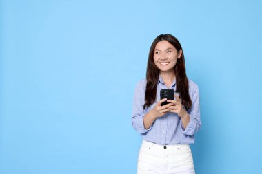 Açık mavi arka planda akıllı telefonu olan gülümseyen bir kadın. Metin için boşluk