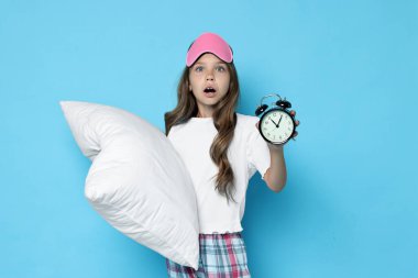 Maskeli, yastıklı ve alarmlı açık mavi arka planda uyuyan kız.