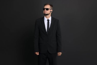 Siyah arka planda güneş gözlüğü takan takım elbiseli genç koruma.