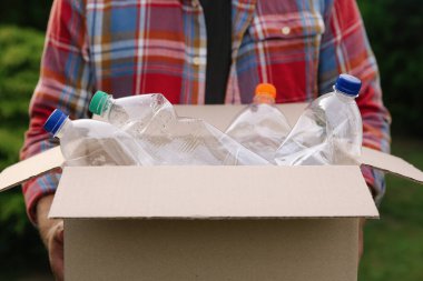 Geri dönüşüm. Elinde plastik şişelerle karton kutu tutan adam, yakın plan.
