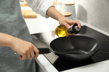 Mutfakta bir şişe yağ ve kızartma tavası olan kadın, yakın plan.