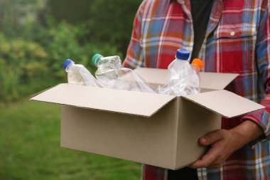 Geri dönüşüm. Elinde plastik şişelerle karton kutu tutan adam, yakın plan.