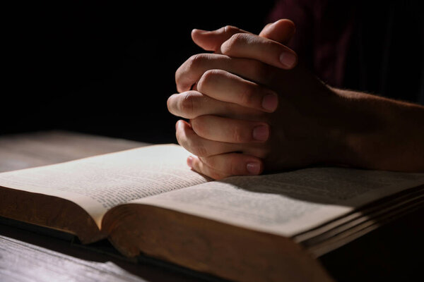 Man with Bible praying at wooden table, closeup