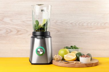 Sarı ahşap masada smoothie için malzeme içeren modern blender.