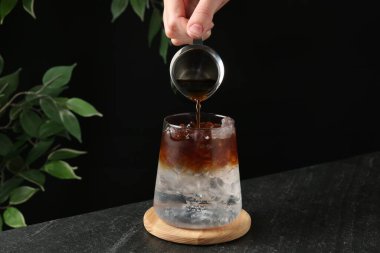 Karanlık masada ferahlatıcı espresso tonik yapan kadın, yakın plan.