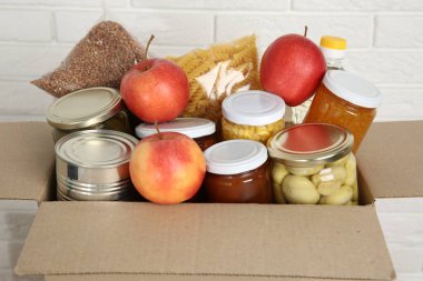 Beyaz tuğla duvarın yanındaki kutuda bağış yapmak için farklı gıda ürünleri.