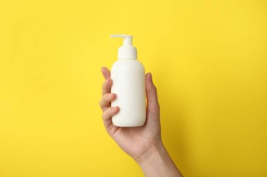 Sarı arka planda şampuan şişesi olan kadın, yakın plan.