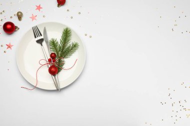 Beyaz arka planda tabak, çatal bıçak takımı ve şenlik dekoruyla Noel sofrası. Metin için boşluk