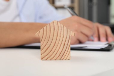 Emlak sigortası. Işık masasında bir şeyler yazan adam, ahşap ev figürüne odaklan.