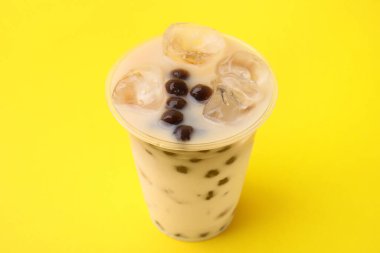 Sarı arka planda plastik bardakta lezzetli sütlü çay, yakın plan.