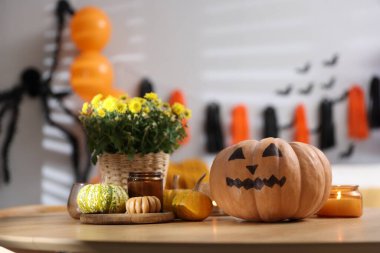 Cadılar Bayramı kutlaması. Ürkütücü yüzlü balkabağı, çiçekler ve mumlar ahşap masada.