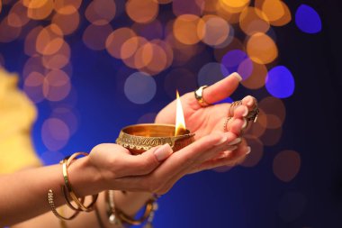 Diwali kutlaması. Renkli arka planda yanan diya lambasını tutan bulanık ışıklı kadın, yakın plan