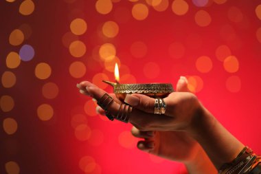 Diwali kutlaması. Kırmızı arka planda yanan diya lambasını tutan bulanık ışıklı kadın, yakın plan.